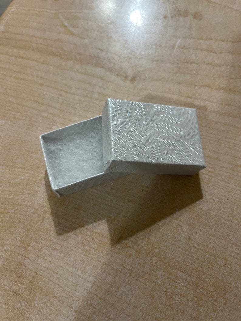 May include: A small, white, rectangular box with a textured, swirling pattern on the lid. The box is open and empty.