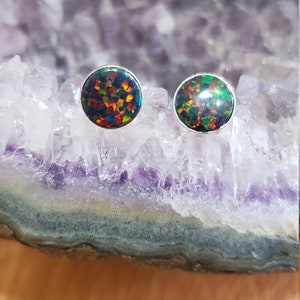 May include: A pair of silver stud earrings with round black opal stones. The opals have a rainbow of colors, including green, red, and blue.