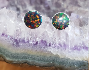 May include: A pair of silver stud earrings with round black opal stones. The opals have a rainbow of colors, including green, red, and blue.