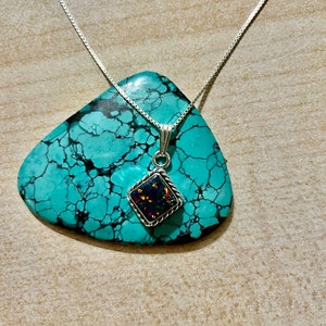 May include: A silver chain necklace with a square pendant featuring a dark iridescent opal stone.