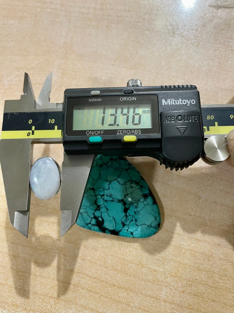 Puede incluir: Un primer plano de un calibre digital que mide una piedra turquesa. El calibre muestra 13,46 mm.
