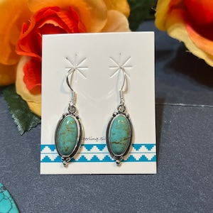 May include: A pair of silver earrings with oval turquoise stones. The earrings are on a white card with the text "Sterling Si" visible.