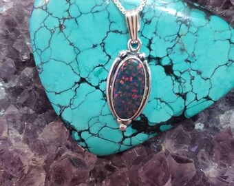 May include: A silver chain necklace with an oval-shaped opal pendant set in a silver bezel. The pendant is surrounded by a decorative silver border. The necklace is displayed on a bed of purple amethyst crystals and a turquoise stone.