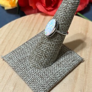 May include: A silver ring with an oval-shaped white opal gemstone. The ring is on a fabric ring holder.