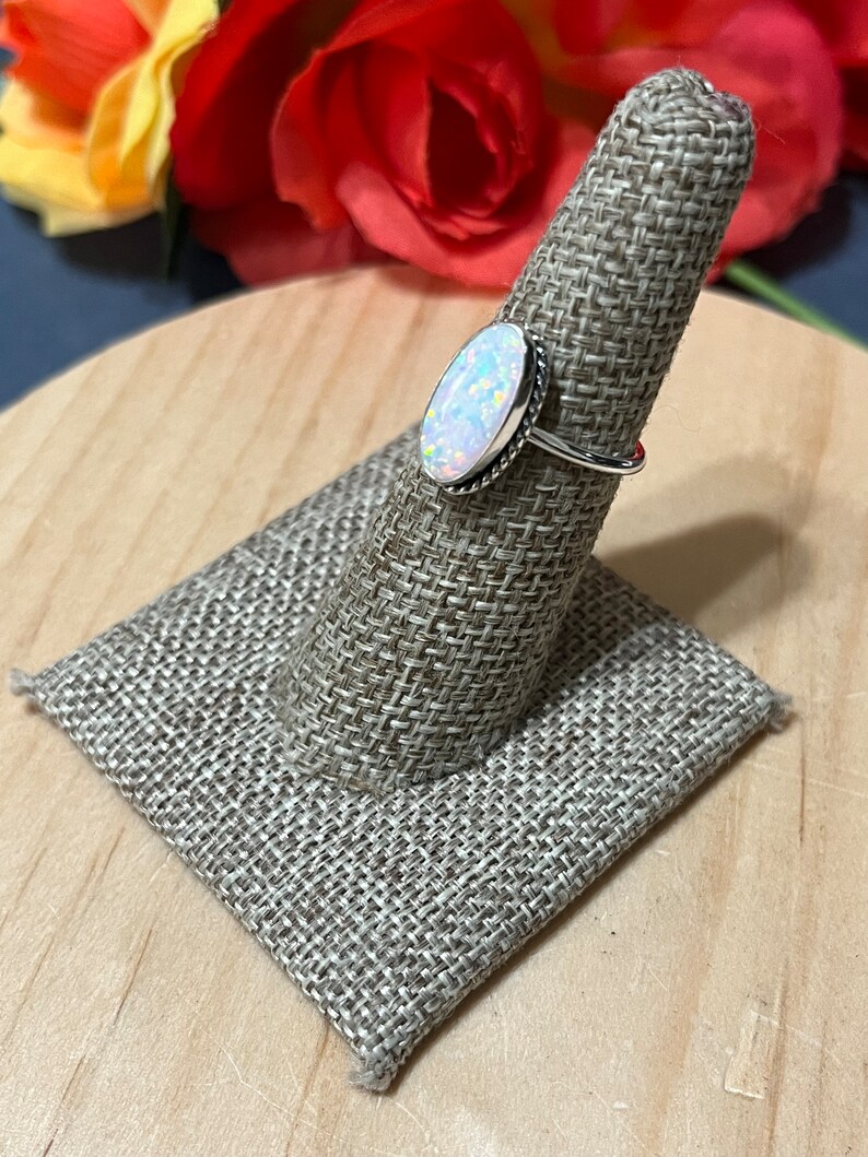 May include: A silver ring with an oval-shaped white opal gemstone. The ring is on a fabric ring holder.