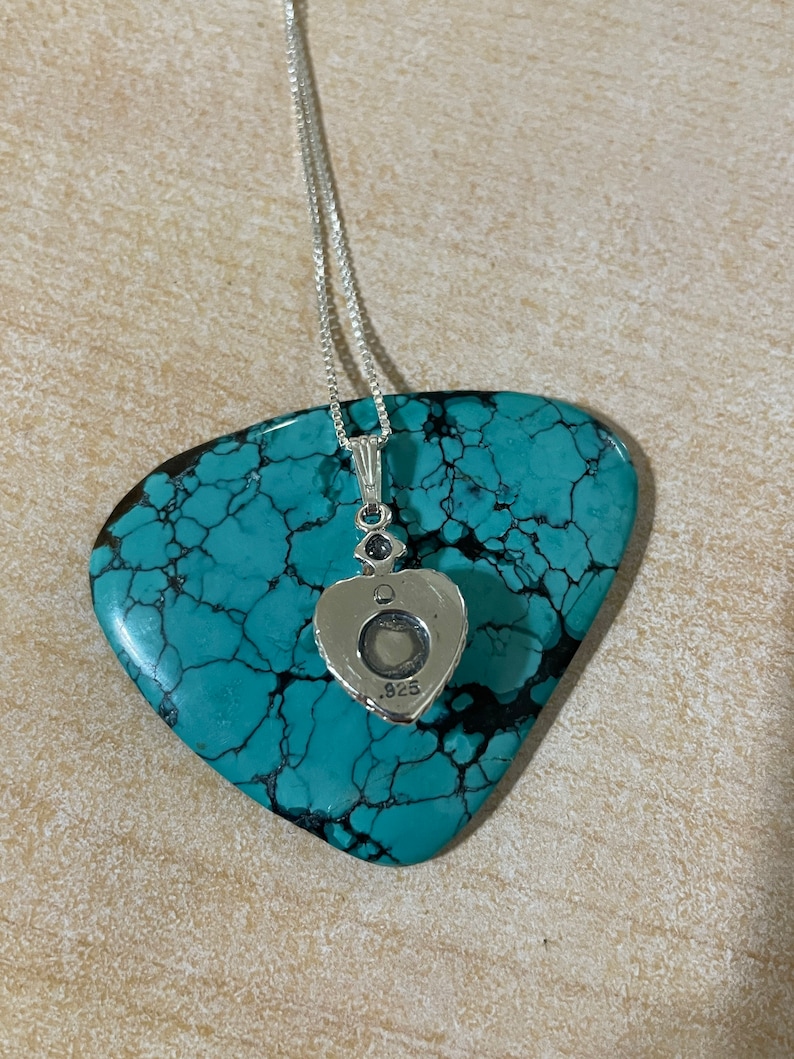 May include: A silver heart-shaped pendant necklace with a small clear stone in the center. The back of the pendant is stamped with ".925".
