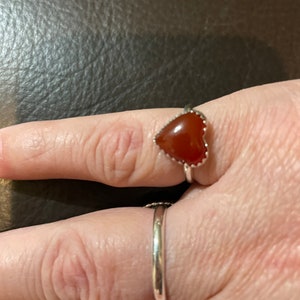 May include: A silver ring with a heart-shaped carnelian stone.