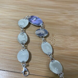 May include: Sterling silver bracelet featuring oval-shaped, iridescent mother-of-pearl stones. The bracelet has a lobster clasp closure and is linked with small silver rings. The stones have a pearlescent sheen, reflecting shades of white and purple.