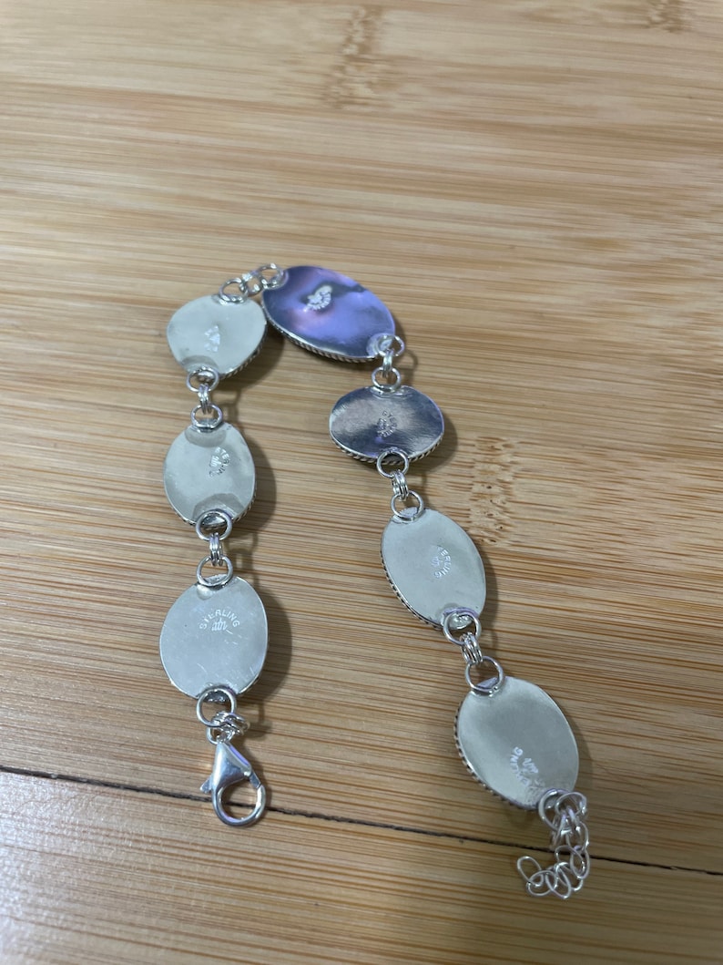 May include: Sterling silver bracelet featuring oval-shaped, iridescent mother-of-pearl stones. The bracelet has a lobster clasp closure and is linked with small silver rings. The stones have a pearlescent sheen, reflecting shades of white and purple.