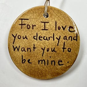 May include: A round, ceramic ornament with a crackle glaze finish. The ornament has the text "For I love you dearly and want you to be mine." A natural twine loop is at the top for hanging.