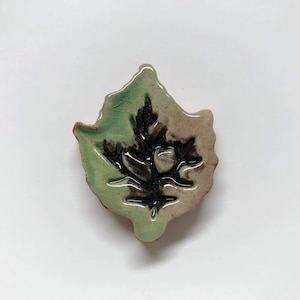 May include: A ceramic leaf-shaped dish with a green glaze and a black silhouette of a leaf in the center.