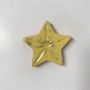 May include: A yellow ceramic star with a raised, textured design. The star is a decorative object.