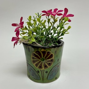 May include: A white ceramic mug with a black handle and the text "But First, Coffee" in a black, handwritten-style font. The mug is on a white surface.