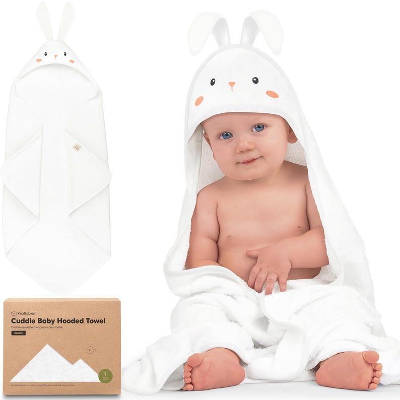 May include: A white baby hooded towel with a bunny face design on the hood. The towel is wrapped around a baby. The packaging box is visible, with the text "Cuddle Baby Hooded Towel".