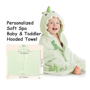 May include: A light green baby and toddler hooded towel with a dinosaur design. The towel measures 43 inches (110cm) wide and 32 inches (80cm) long. The hood has a green spike and embroidered name "Finley". The text "Personalized Soft Spa Baby & Toddler Hooded Towel" is also visible.