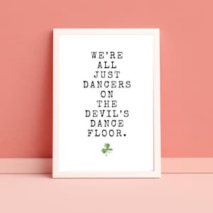 May include: White framed print with black text that reads "We're all just dancers on the devil's dance floor." A green shamrock is at the bottom of the print.