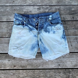May include: Light blue denim shorts with distressed details and a bleached effect. The shorts have a frayed hem and a button fly.