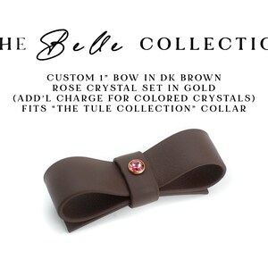 May include: Dark brown leather bow, approximately 1 inch, with a small rose-colored crystal in a gold setting.  The text on the image reads: 'THE Belle COLLECTION', 'CUSTOM 1' BOW IN DK BROWN ROSE CRYSTAL SET IN GOLD (ADD'L CHARGE FOR COLORED CRYSTALS) FITS 'THE TULE COLLECTION' COLLAR.  The bow is a decorative accessory, suitable for collars or other apparel.