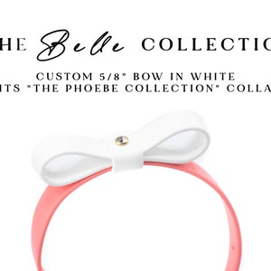 May include: The Belle Collection: Custom 5/8' white bow, shown on a coral headband.  The bow features a small, clear rhinestone accent.  This accessory is designed to fit The Phoebe Collection collar.  The text 'THE Belle COLLECTION' is displayed above the product image. The text 'CUSTOM 5/8' BOW IN WHITE' and 'FITS 'THE PHOEBE COLLECTION' COLLAR' are also displayed.