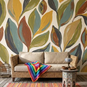 May include: A living room scene featuring a beige wicker sofa with a colorful, rainbow-patterned blanket. The wall behind the sofa is painted with large, stylized leaves in shades of yellow, green, blue, and brown. A striped rug and decorative table complete the scene.
