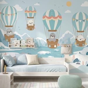 May include: A light blue wall mural featuring four hot air balloons carrying a seal, a bear, another seal, and a fox over a snowy landscape with mountains and an igloo. A light wood daybed with blue and beige pillows sits in front of the wall.