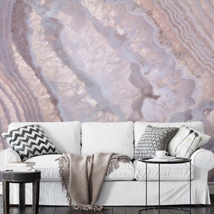 Può includere: Un divano bianco con una coperta e cuscini in un soggiorno con un murale a parete con motivo di agata rosa e bianca.