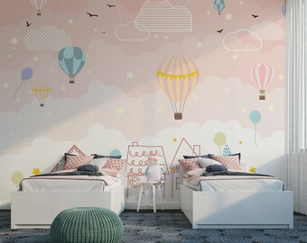 Könnte beinhalten: Kinderzimmer mit einem rosa-weißen Wandbild mit Heißluftballons, Wolken und Sternen. Zwei weiße Betten mit gemusterten Kissen und ein grüner Hocker befinden sich vor dem Wandbild. Ein skurriles und farbenfrohes Design.