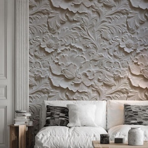 Può includere: Un pannello murale a rilievo floreale bianco con un design dettagliato e strutturato. Il pannello presenta grandi fiori e foglie stilizzate. Un divano bianco con cuscini e un tavolino in legno sono di fronte al muro.