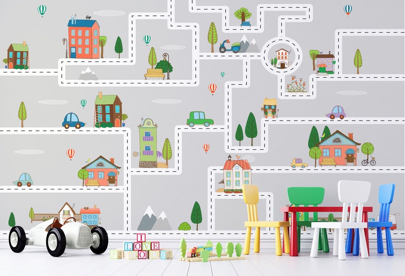 May include: A children's playroom with a gray wall mural depicting a city with roads, houses, cars, trees, and hot air balloons. There are four colorful chairs and a red table in front of the mural.  On the floor are wooden blocks that spell out 'I LOVE YOU' and a toy car.