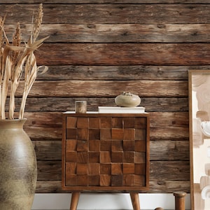 May include: A wooden cabinet with a geometric design on the front, set against a rustic wood-paneled wall. A large vase with dried plants and a framed artwork are also visible, creating a warm, inviting interior design scene.