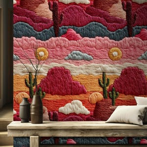 Könnte beinhalten: Gestickte Wandkunst, die eine Wüstenlandschaft mit Kakteen, Bergen und Wolken in Rot-, Orange-, Rosa- und Blautönen zeigt. Das Kunstwerk befindet sich über einer Holzbank mit Vasen.