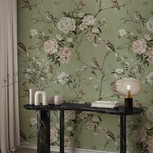 Op de afbeelding: Een zwarte marmeren consoletafel met een gebogen blad en twee poten. De tafel is versierd met een vaas, een sculptuur en een lamp. De achtergrond is een groene behang met een bloemenpatroon en vogels.