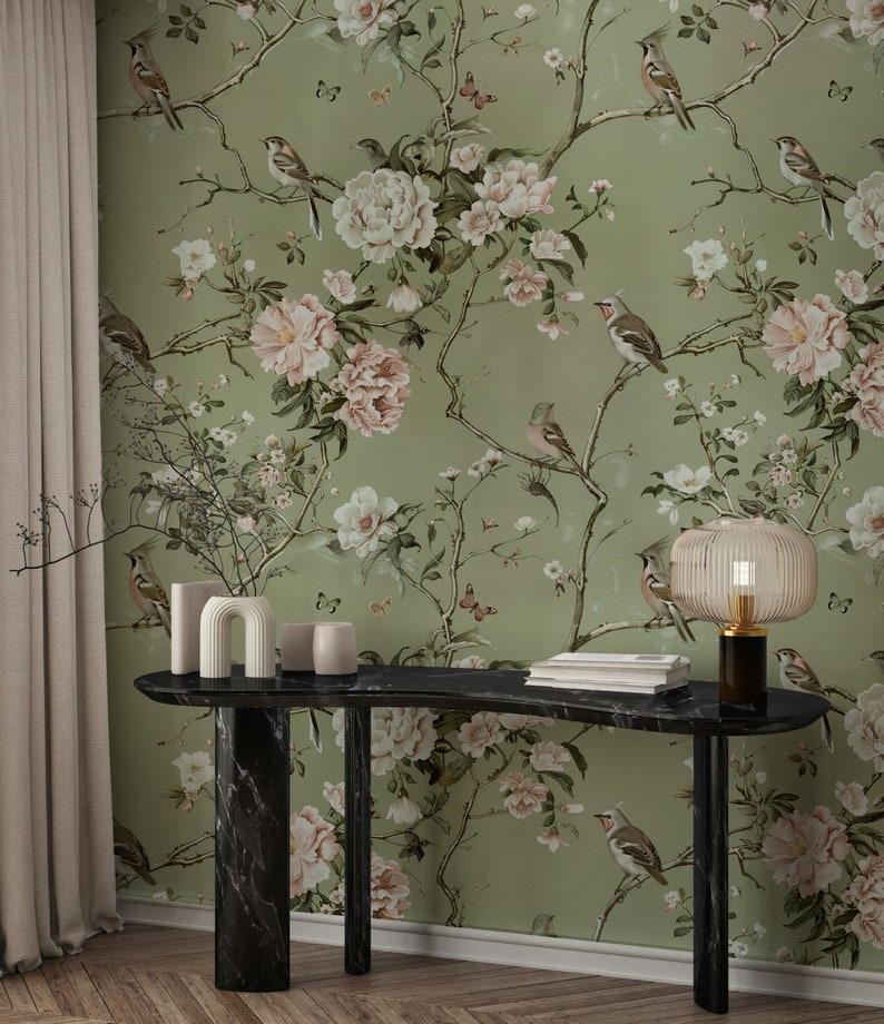 Op de afbeelding: Een zwarte marmeren consoletafel met een gebogen blad en twee poten. De tafel is versierd met een vaas, een sculptuur en een lamp. De achtergrond is een groene behang met een bloemenpatroon en vogels.