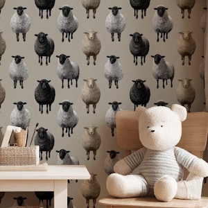 Op de afbeelding: Een kinderkamer met beige behang met een patroon van zwarte, grijze en bruine schapen. Een witte teddybeer met grijze strepen zit op een houten stoel. Een kleine witte tafel en een mand staan op de voorgrond.