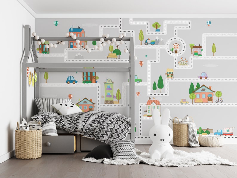 May include: A child's bedroom with a gray loft bed and a white rabbit stuffed animal. The wall behind the bed has a gray and white wallpaper with a road and city theme. The wallpaper features houses, cars, trees, and a scooter. The bed has a black and white chevron patterned comforter and a gray and white striped pillow.