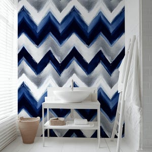 Puede incluir: Un baño moderno con un lavabo blanco y una pared con un patrón de chevrón azul y blanco. La habitación tiene pisos de madera blancos, una cesta tejida y un toallero blanco. El patrón de la pared es un diseño audaz.