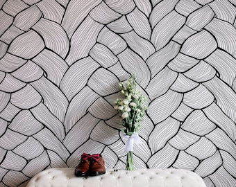 Op de afbeelding: Een witte bank met een gestoffeerde zitting staat voor een muur met een zwart-wit abstract patroon. Een boeket witte bloemen in een vaas en een paar bruine leren schoenen met rode strikken staan op de bank.