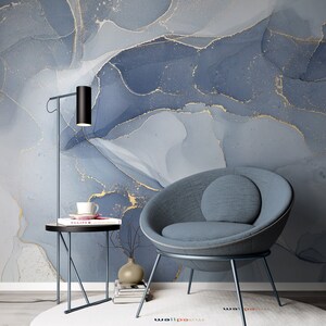 May include: A blue and gold abstract marble wallpaper with a blue armchair and a black side table with a book and a cup on top. The side table has a black metal frame and a round top. The armchair has a round back and a gray fabric seat. The wallpaper has a modern and abstract design.