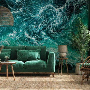 Könnte beinhalten: Ein Wohnzimmer-Interieur mit einem grünen Samtsofa, einem Korbstuhl, einem Holz-Beistelltisch und einer grünen Pflanze. Die Wand ist mit einer großflächigen Tapete verziert, die ein abstraktes Muster aus blauen und weißen Ozeanwellen zeigt.