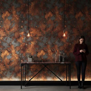 May include: A textured wall with a mottled pattern in shades of copper, rust, and gray. A black metal console table with a marble top holds decorative bottles and a small potted plant. Two hanging light bulbs illuminate the scene.