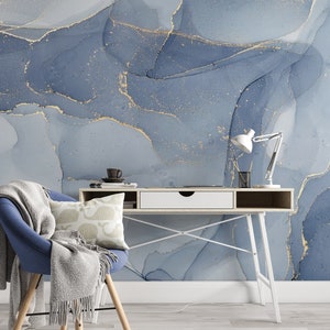 May include: A white desk with a white drawer and a blue chair with a gray throw blanket. The desk has a white metal frame and is set against a wall with a blue and gold abstract design.