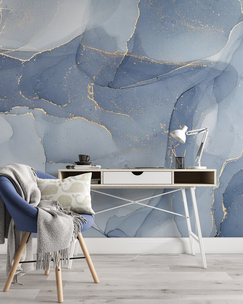 May include: A white desk with a white drawer and a blue chair with a gray throw blanket. The desk has a white metal frame and is set against a wall with a blue and gold abstract design.