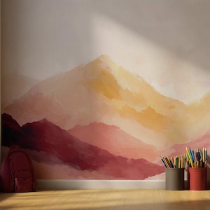 Könnte beinhalten: Ein Wandbild mit einer Bergkette in Rot-, Orange- und Gelbtönen. Ein weinroter Rucksack liegt auf dem Boden. Drei Behälter enthalten Buntstifte. Links ist ein Fenster zu sehen.
