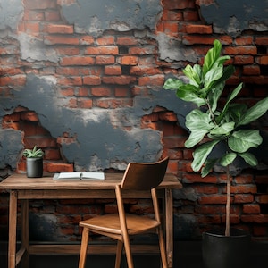 May include: A rustic home office setup featuring a wooden desk and chair against a brick wall with peeling paint. A small potted plant and a notebook sit on the desk. A large potted plant is on the right.