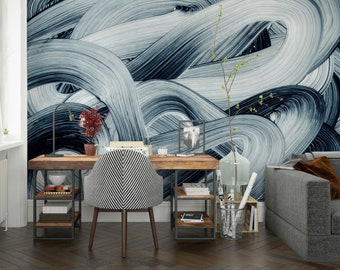 Op de afbeelding: Een thuiskantoorwerkplek met een houten bureau en een zwart-wit gepatroneerde stoel. De muur achter het bureau is versierd met een blauw en wit abstract schilderij. Er zijn planken en een lamp op het bureau, evenals een vaas met bloemen en een glazen pot met opgerolde papieren.