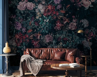 Può includere: Un divano in pelle marrone scuro con una coperta a chevron si trova di fronte a un muro con una carta da parati floreale scura. Una lampada da terra dorata e un piccolo tavolo rotondo con libri sono anche nella stanza.