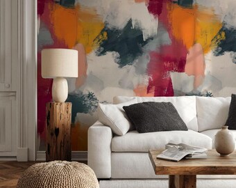May include: An abstract art wallpaper in a living room setting. The wall features large brushstrokes in shades of red, orange, yellow, white, and teal. A white sofa, wooden coffee table, and a beige pouf are in the foreground.