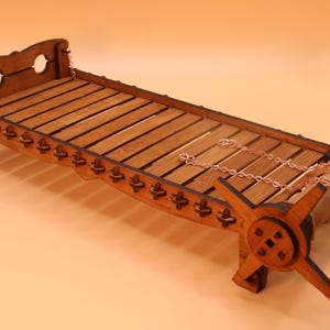 Op de afbeelding: Een houten bedframe met een lattenbodem en een decoratieve metalen ketting. Het bedframe heeft een uniek ontwerp met ingewikkelde houtsnijwerk en een afgerond hoofdeinde.