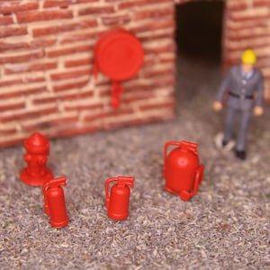 Op de afbeelding: Een set miniatuur brandveiligheidsuitrusting, waaronder een brandkraan, brandblussers en een brandalarm. De items zijn rood en gemaakt van plastic.