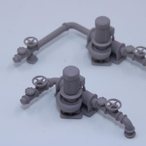 May include: Two miniature grey industrial pump assemblies featuring vertical motors, connected piping, and circular hand-operated valves. These detailed models are cast in a solid matte grey material, showcasing complex mechanical components and plumbing.